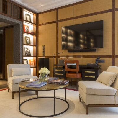 Le salon de l'une des chambres de l'hôtel Portrait Milano, avec coin télé, deux fauteuils beiges, une table basse ronde et une bibliothèque en bois