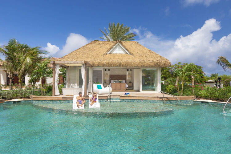 Une villa chapeautée de palme, entourée de palmiers, au bord d'une grande piscine turquoise