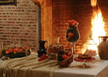 Une table chargée de coupes et de paniers de fruits et légumes d'automne, dressée devant un feu de cheminée au Clos Lucé