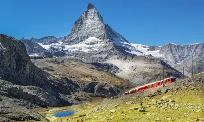 Voyages d'exception en train: vue d'un train grimpant une côte en Suisse, avec en arrière plan, un superbe pic rocheux
