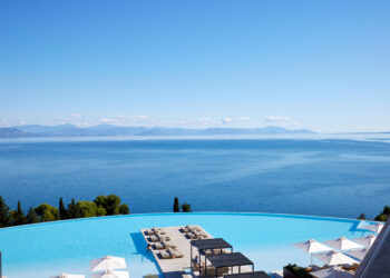 Vue d'une piscine en arrondi entourée de transats avec vue sur la mer Ionienne à l'Angsana Corfou Resort & Spa