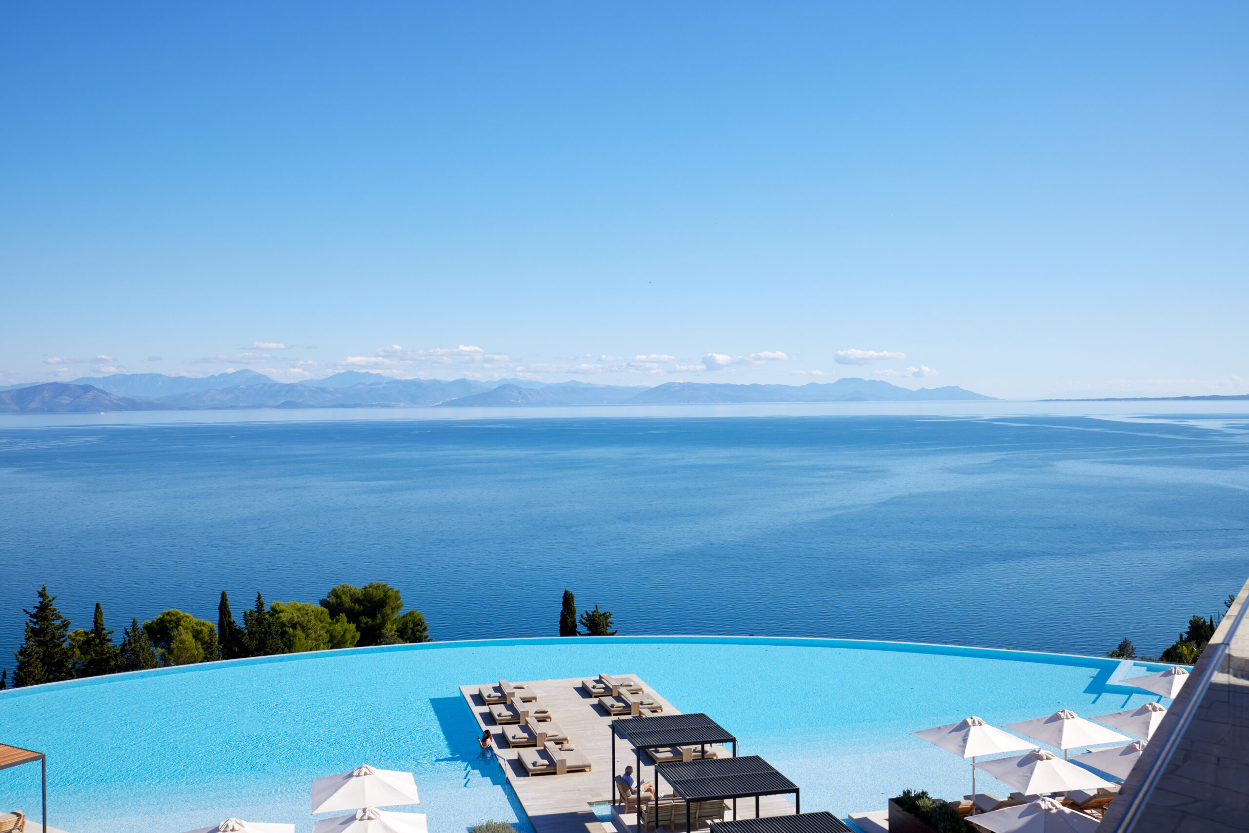 Vue d'une piscine en arrondi entourée de transats avec vue sur la mer Ionienne à l'Angsana Corfou Resort & Spa